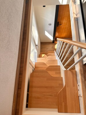 A wooden staircase with a handrail, leading to a landing with a door and a window.