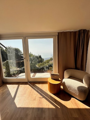 A room with a large sliding glass door, a round wooden side table, and a beige sofa.