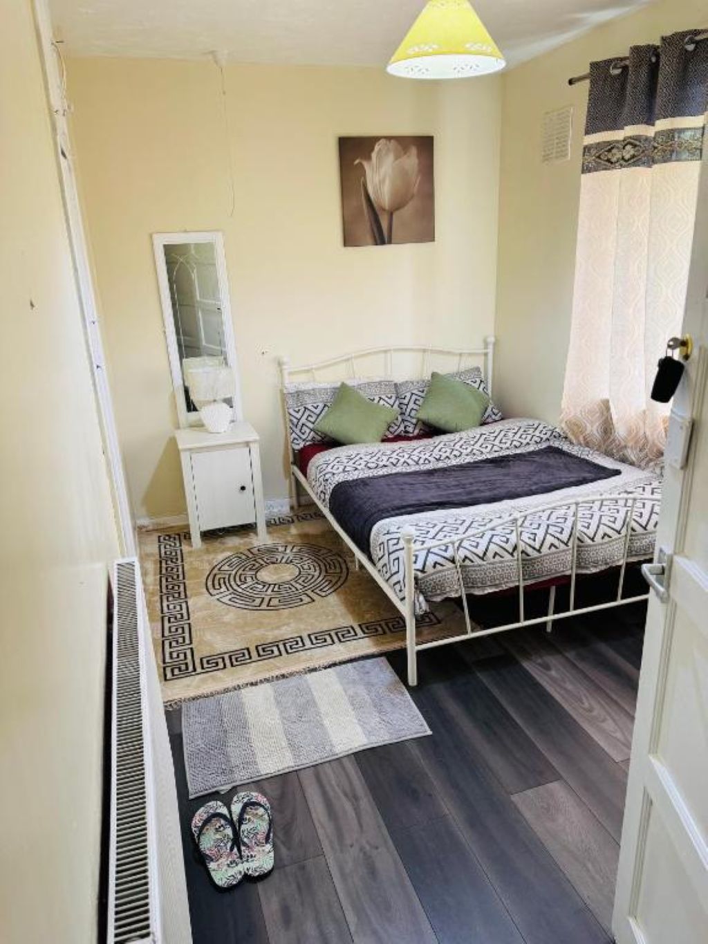 A bedroom with a bed, a nightstand, a mirror, a painting, and a patterned rug.