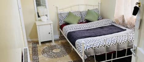 A bedroom with a bed, a nightstand, a mirror, a painting, and a patterned rug.