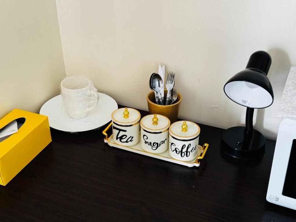 A desk with a tissue box, a mug, a tea and coffee canister set, a spoon holder, and a desk lamp.