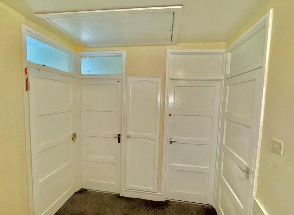 Corredor com portas brancas, luminária no teto e uma tomada visível.