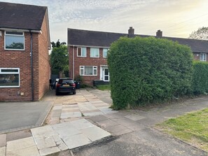Une rue résidentielle bordée de maisons, avec une voiture garée et une haie.