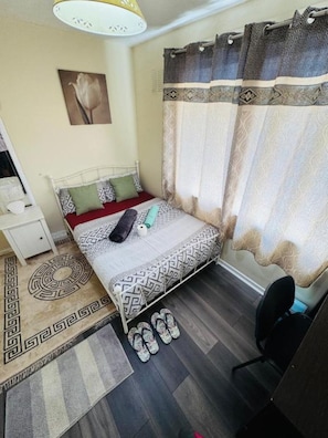 Ein Schlafzimmer mit einem Bett, einem Schreibtisch, einem Stuhl, einer Lampe und einem gemusterten Teppich.