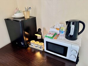 Eine Küchenzeile mit einer Mikrowelle, einem Wasserkocher, einer Kaffeemaschine und einem Kaffeetassen-Set.