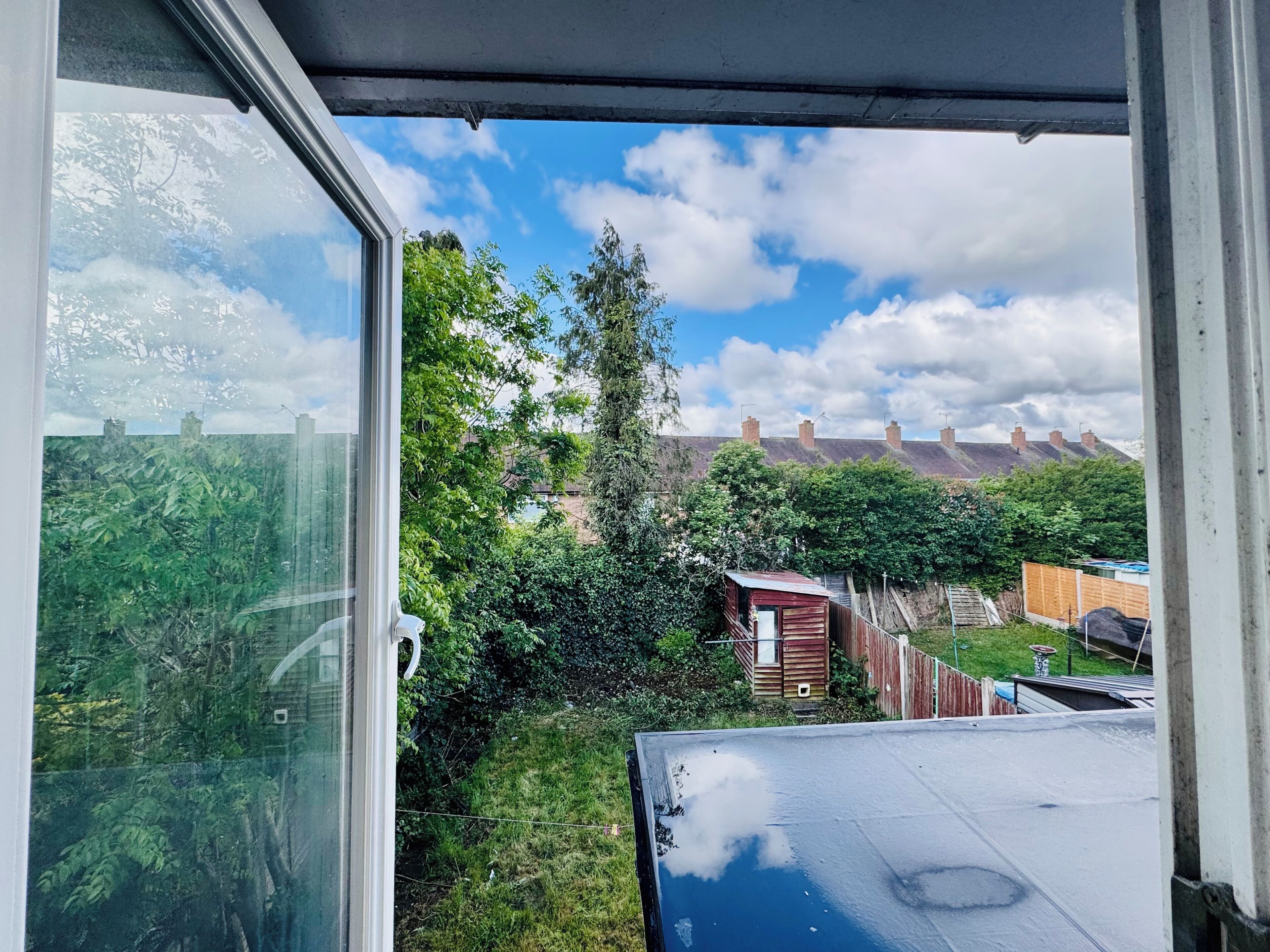 A view through a window with a clear sky, a grassy area, and a red building in the distance.