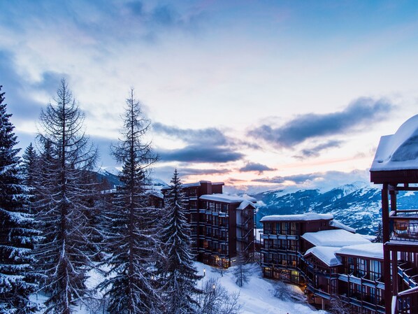 A snow-covered lodge with multiple buildings, surrounded by snow-laden trees and mountains in the background.
