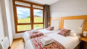 Habitación de hotel con dos camas, un ventanal con vistas a un campo césped y un edificio, y un cabecero de madera.