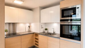 Cocina moderna con armarios blancos, electrodomésticos de acero inoxidable y horno empotrado.