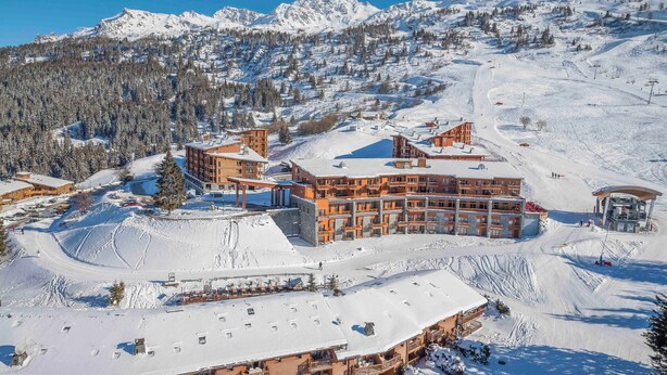 Un hotel de varios pisos con una pista de esquí al fondo.