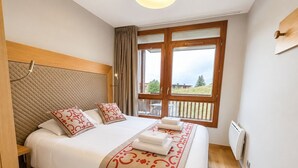 A hotel room with a bed, a window with a view, a wooden headboard, and a bedside table.
