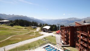 A mountain resort with a pool, a building with balconies, and a clear view of the surrounding mountains.