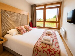 A hotel room with a large bed, a TV, a window with a view, and a red chair. - T4 au pied des pistes | Accès piscine | Balcon (Bourg-Saint-Maurice)