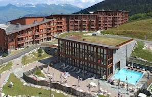 A hotel with a rooftop pool, multiple balconies, and a view of mountains.
