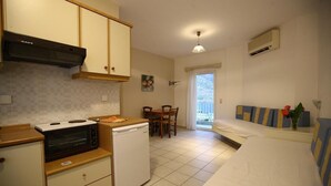 A compact kitchen with a stove, microwave, and dishwasher, a dining area with a table and chairs, and a bed with a view of the outdoors. - Ormos Atalia Village (Mylopotamos)