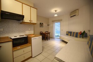 A compact kitchen with a stove, microwave, and dishwasher, a dining area with a table and chairs, and a bed with a view of the outdoors.