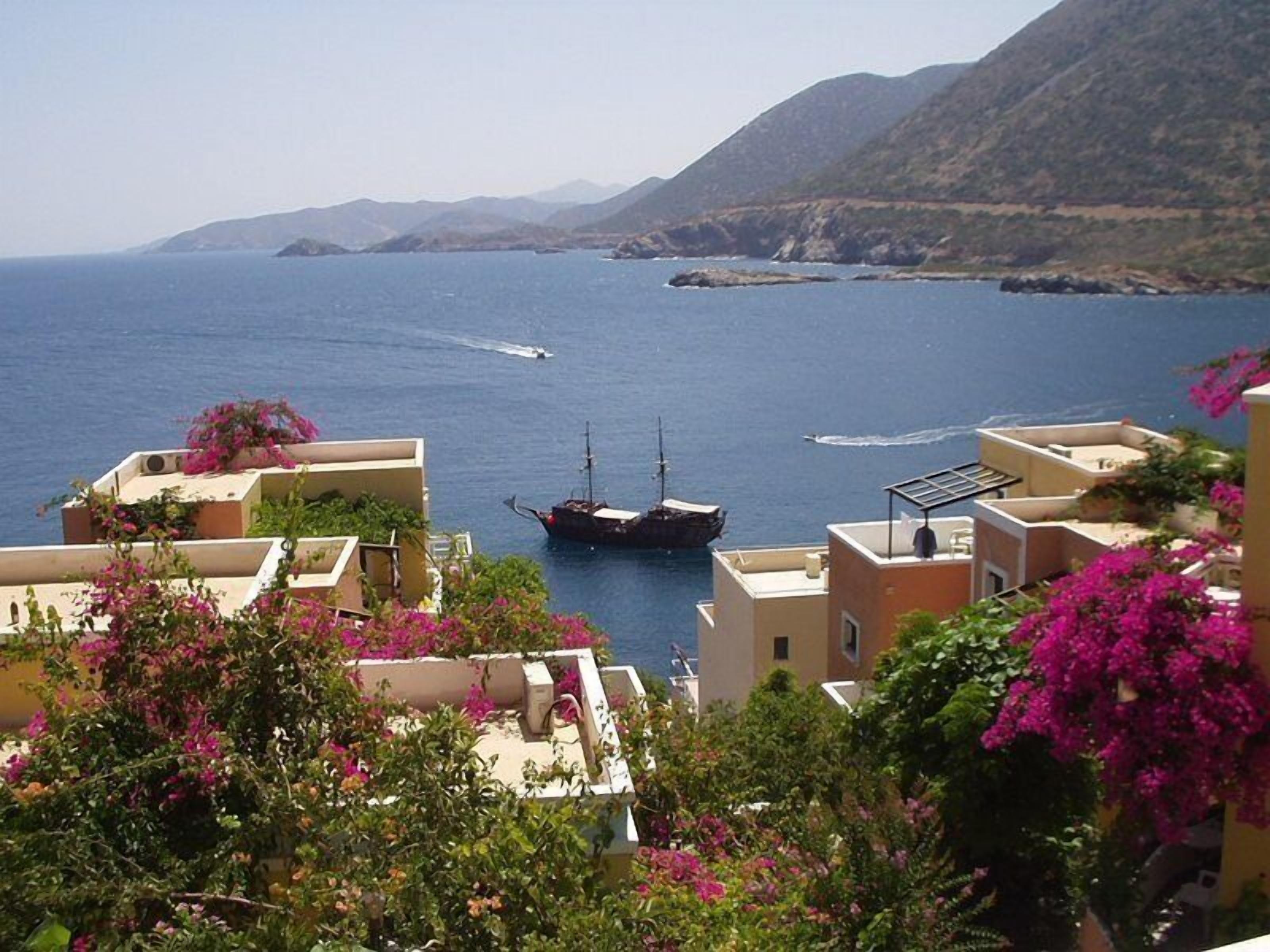 A coastal town with buildings, a boat, and a mountainous backdrop.