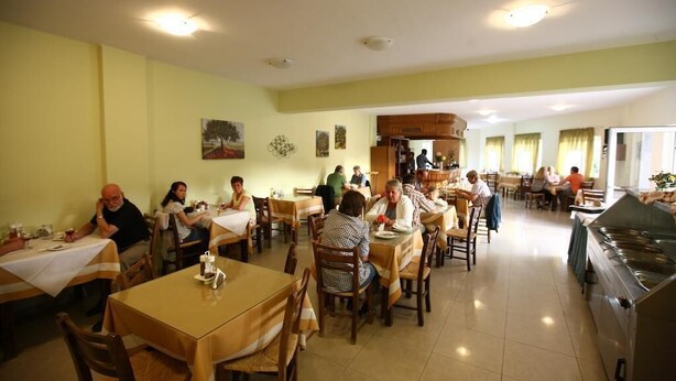 A dining area with multiple tables and chairs, a kitchen area, and a counter with a stove. - Ormos Atalia Village (Mylopotamos)