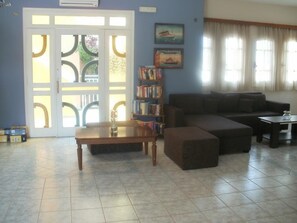 A living room with a sectional sofa, a coffee table, a bookshelf, and a door with a glass panel. - Ormos Atalia Village (Mylopotamos)