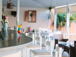 Un área de bar con un cóctel sobre la barra, sillas blancas y un comedor al fondo.