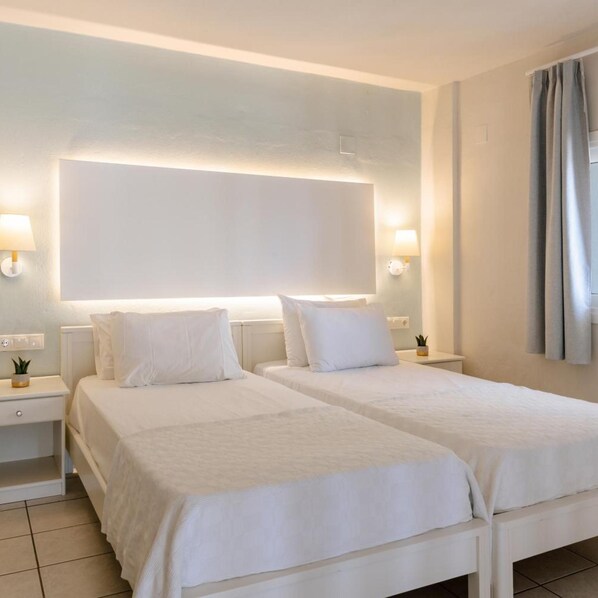 Habitación de hotel con dos camas, mesitas de noche, un espejo grande y vista al mar.