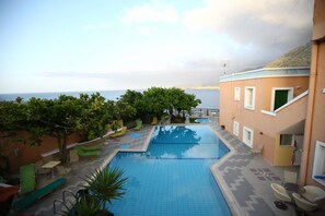 Una piscina con sillones de descanso y vista al mar.