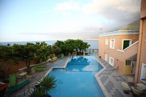 Una piscina con sillones de descanso y vista al mar.