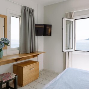 A bedroom with a bed, a desk with a chair, a television, and a window with curtains.