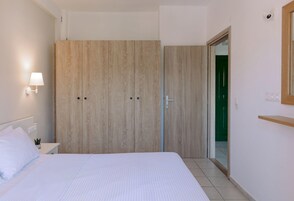 Un dormitorio con cama, armario, mesita de noche, lámpara y puerta que da a otra habitación.