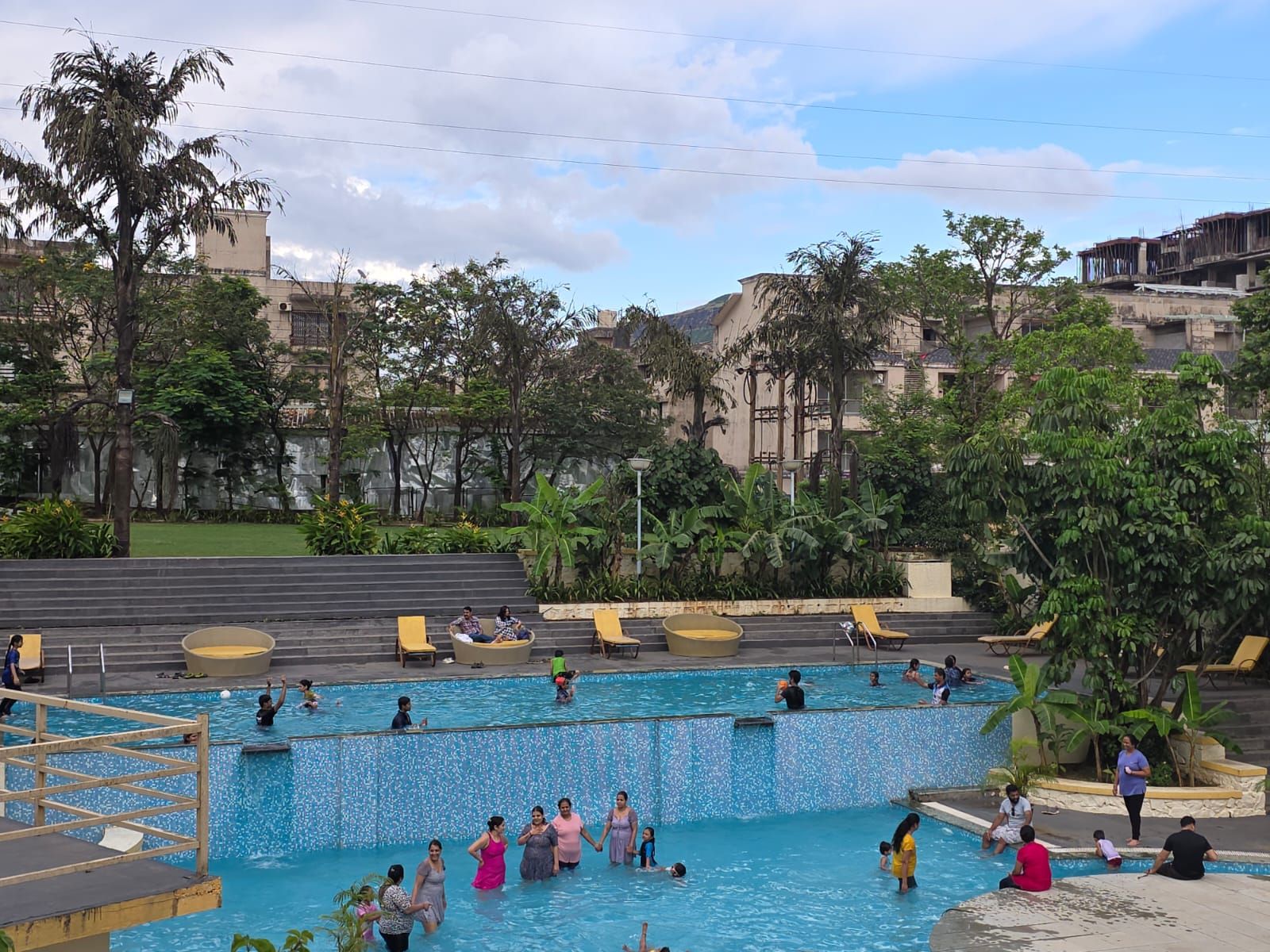 A swimming pool with people, surrounded by trees and buildings.