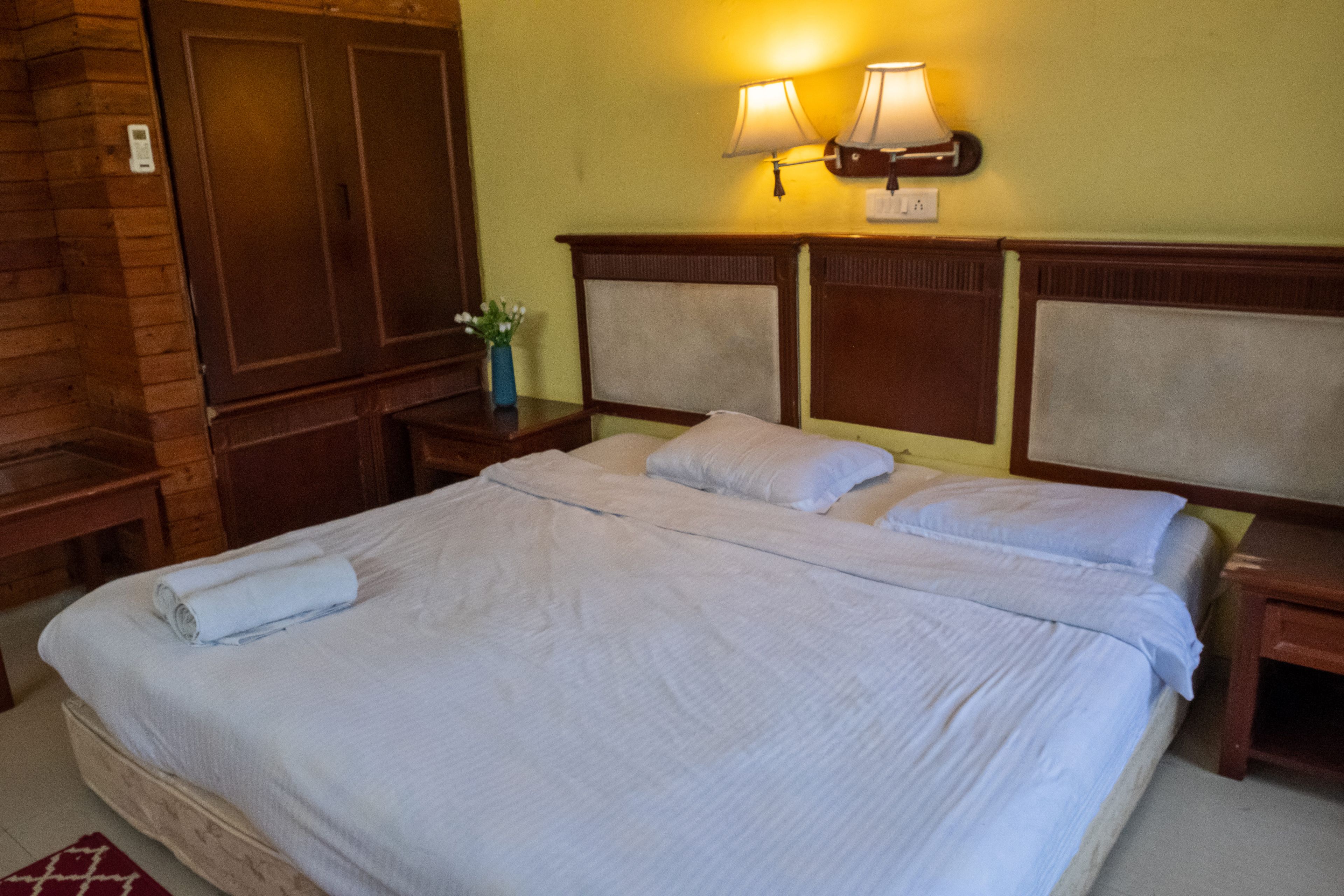 A hotel room with a large bed, two bedside tables, a nightstand with a lamp, and a wall-mounted light fixture.