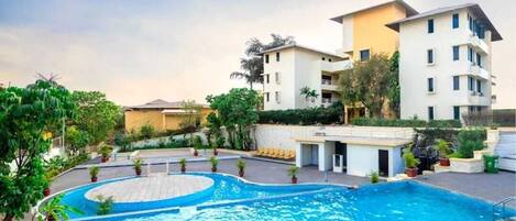 A hotel with a swimming pool, multiple floors, and surrounding greenery.
