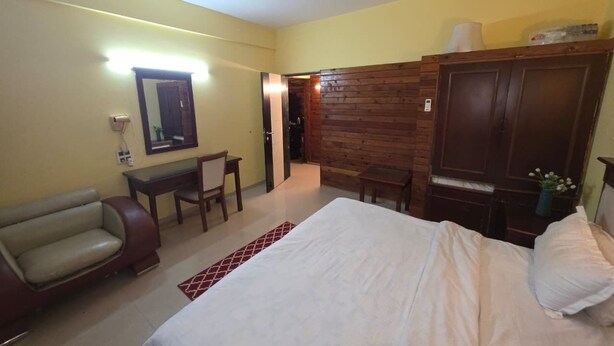 Una habitación de hotel con cama, escritorio, silla, armario y ventilador de techo.