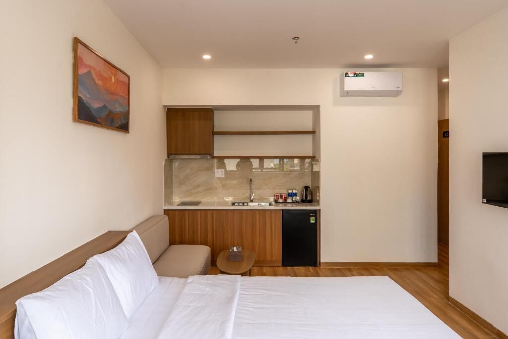 A hotel room with a bed, a small kitchenette, a TV, and a painting on the wall.
