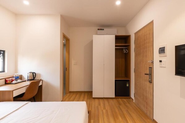 Habitación de hotel con cama, escritorio, silla, armario y televisor.