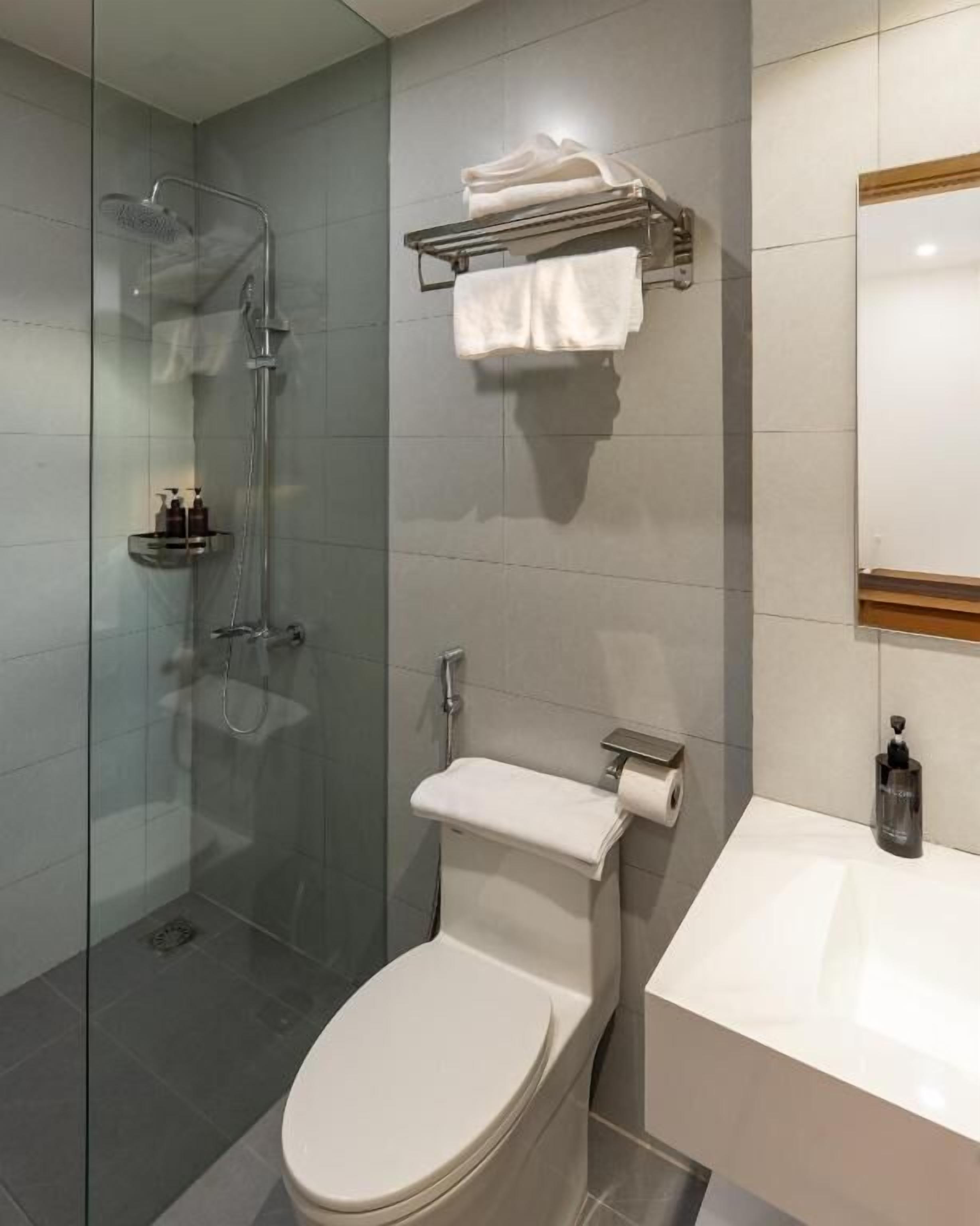 Un baño moderno con ducha envuelta en vidrio, inodoro y lavabo con espejo arriba.