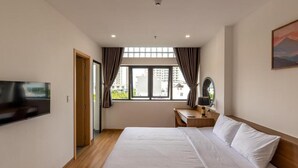 Quarto de hotel com cama, escrivaninha, cadeira, televisão e janela com cortinas.