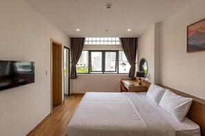 Habitación de hotel con cama, escritorio, silla, televisión y ventana con cortinas.