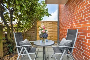 Een terras met twee stoelen en een tafel, een houten schutting en een bakstenen muur.