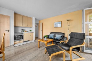 A compact living space with a kitchenette, a sofa, a coffee table, and a chair. - Modern beachfront apartment with exceptional sea views at Schönberger Strand (Schönberg (Holstein))
