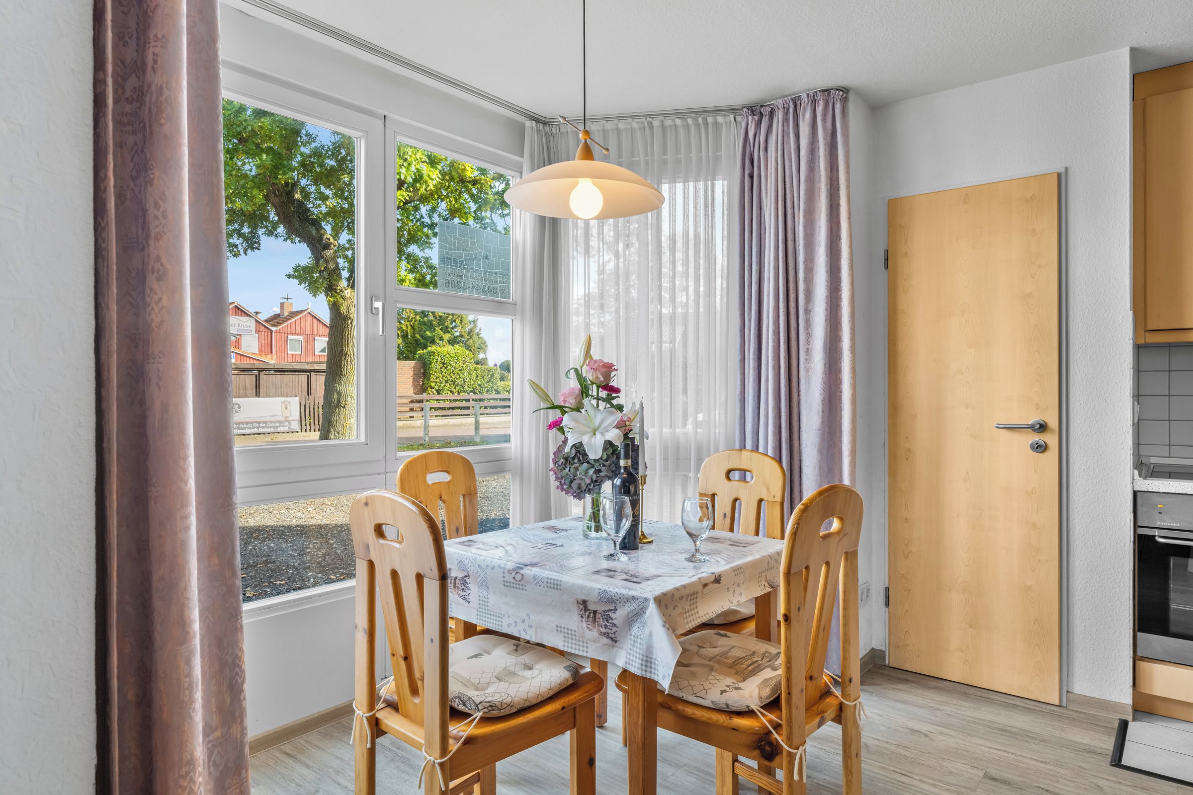 Un comedor con una mesa dispuesta para dos personas, sillas de madera, una lámpara colgante y vistas al exterior a través de amplios ventanales.