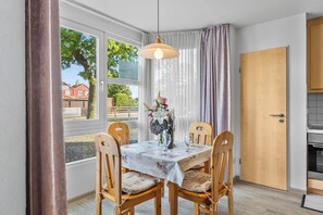 Un comedor con una mesa dispuesta para dos personas, sillas de madera, una lámpara colgante y vistas al exterior a través de amplios ventanales.