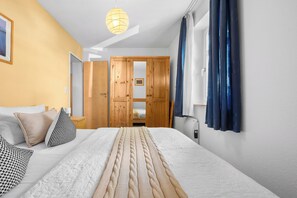 Une chambre à coucher comprenant un lit, des oreillers, une table de chevet, un luminaire suspendu, une armoire et une fenêtre avec des rideaux.