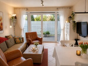 Ein Wohnzimmer mit einer Couch, Sesseln, einem Couchtisch mit einer Kerze und einem Fernseher.