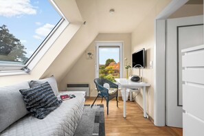 A cozy room with a sloped ceiling, a bed with a quilted cover, a chair, a small table with a lamp, and a TV mounted on the wall. - Küstenperle – Your Cozy Holiday Home for a Relaxing Getaway (Schönberg (Holstein))