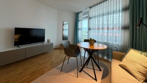 A modern living room with a flat-screen TV, a dining table with chairs, a sofa, and a large window with curtains. - Romantic lakeside cabin with a balcony and indoor communal pool in Uhldingen-Mühlhof (Uhldingen-Mühlhofen)