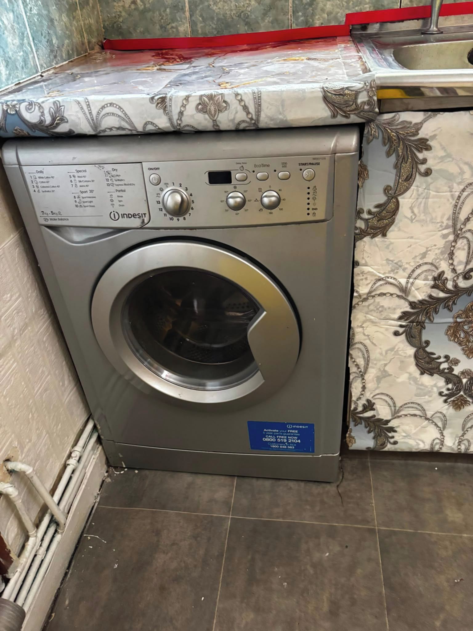A front-loading washing machine with a control panel, a label, and a decorative backsplash.