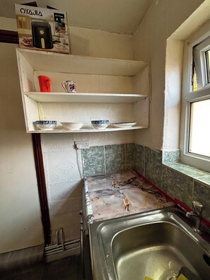 A kitchen with a stainless steel sink, a window, and a shelf above the countertop.
