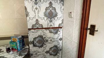 Una habitación de esquina con papel tapiz estampado, una puerta de madera y una mesa con objetos encima.