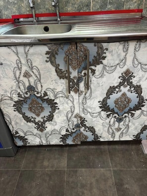 A kitchen with a stainless steel sink, a red countertop, and decorative cabinet doors with intricate patterns.